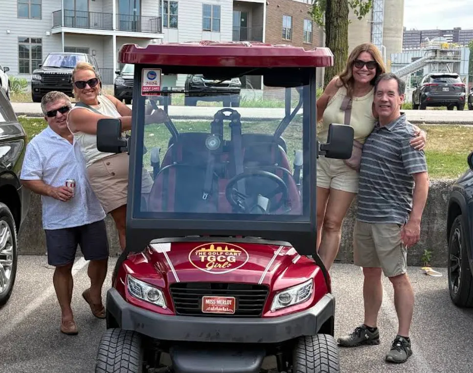 Friends posing around a red The Golf Cart Girl-CLE cart during a Cleveland ride